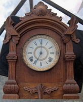 Front view of the Gothic oak wood cased clock showing the round clock face with Roman numerals and carved wood details framing the clock.