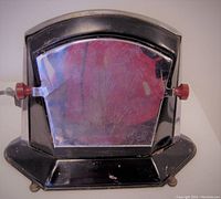 Front view of Art Deco toaster showing black body, chrome panel with etched design, and cherry red Bakelite knobs on each side.