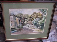 Framed watercolor painting showing Old English Cotswold village street with a pub and cottages, matted and framed.