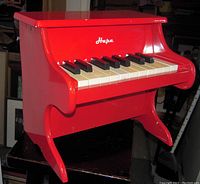 Red child's piano with 18 black and white keys, Hape logo visible.