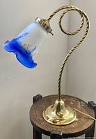 Photo of French Art De France desk lamp showing twisted brass arm, flower-shaped glass shade with blue and white design, and round base on wooden surface.