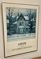 Framed poster showing urban winter scene with house covered in snow and bare trees.