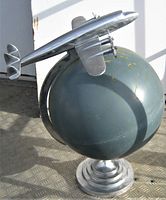 Frontal view of silver metal airplane on green painted globe with stepped base