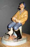 Side view of the seated seafarer figurine showing the figure holding a paper and a white bird near his feet on the base.