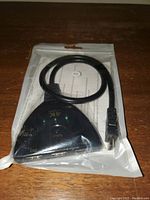 Black 3-input HDMI switch sealed in a clear plastic bag, showing the input ports, LED indicators, and attached HDMI cable.