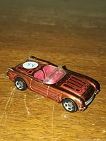 Single diecast toy car modeled after a 1955 Chevrolet Corvette, metallic copper with red interior, on a wooden surface.