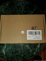Top view of sealed brown cardboard box with handwritten 'BT' and sticker with barcode.