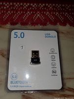 Single photo showing a new USB Bluetooth 5.0 dongle in packaging with branding and compatibility icons.