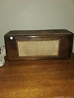 Full front view of the vintage wooden speaker with fabric grille and visible attached white cord.