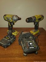Ryobi cordless drill and impact driver, battery charger, and battery laid out on wooden surface