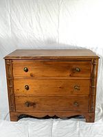 Front view of dresser showing three drawers, brass pulls, fluted side columns and scalloped base.