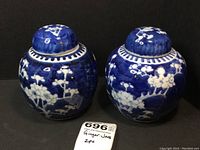 Pair of blue and white ginger jars with cherry blossom patterns on black background; lids on both pieces; one lid has repaired breakage.