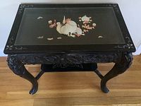 Full view of the dark wooden table with glass top showing inlaid rooster and flowers, hand carved legs and apron.