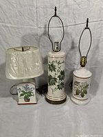 Three ceramic table lamps of different heights with botanical motifs, including one with a white plastic lampshade.
