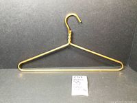 Single gold aluminum hanger displayed against a black background with a small note showing details.
