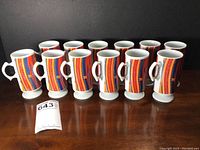Front view of all 12 coffee mugs lined up showing colorful abstract pattern