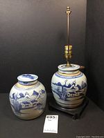 Pair of blue and white ceramic ginger jars side by side, one small jar with lid, the other converted to a lamp with brass fixture, placed on dark wooden stands.