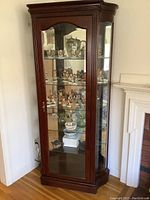 Front and side view of the wooden framed glass curio cabinet showing multiple shelves with display items inside, highlighting the cabinet's structure and glass panels.
