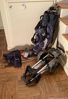 Photo showing golf bag, push cart, and assorted golf clubs on floor near stairs.