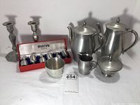 Photo showing all pewter items and candle holders together, including coffee set, teapot, creamer, sugar bowl, shot glasses in box and candlesticks.