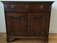 Front view showing full-width drawer with brass ring pulls, two cabinet doors, dentil molding and bracket feet