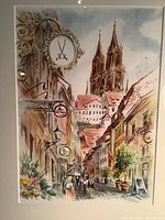 Close-up of framed watercolor print showing detailed street view of Cologne with church spires, people, and flower pots.
