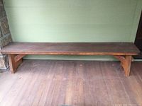 Long wooden outdoor bench from front showing entire length and top surface with rounded and flat edges.