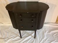 Full front view of the black Martha Washington sewing cabinet with side wings folded out and three drawers visible.