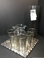 Set including votive holder, six drinking glasses, crystal pitcher, and platter arranged together showing design and size.