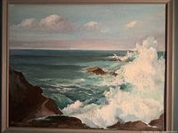 Painting of ocean waves crashing on rocky coast framed in blue-gray wooden frame.