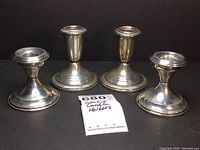 Four sterling silver candle holders arranged side by side on a black background, two taller by Crown Silver Co. and two shorter unmarked, showing general appearance and condition.
