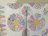 Close-up of middle section showing three Dresden Plate blocks and hand-quilting stitches on white background