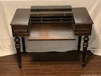 Front view of vintage wooden writing desk with flip-top lid opened horizontally into writing surface and showing closed drawers