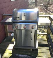 Full front view of stainless steel grill with lid closed, side shelves, cabinet base and wheels