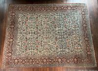Full view of rectangular rug on hardwood floor, showing overall floral pattern and border.