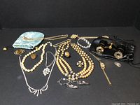Collection of vintage jewelry pieces including multiple necklaces, bracelets, brooches, pouches, wristwatch, and opera glasses.