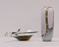 Image showing both art glass pieces side by side: irregular shaped bowl with green and amber tones and pink-green-gray tall vase.
