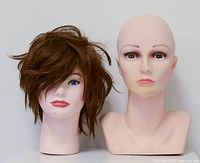 Two vintage life size mannequin heads side by side, one with wig and one bald