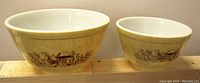 Two vintage Pyrex glass mixing bowls showing mushroom and floral decoration on a yellow speckled background on wooden shelf.