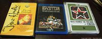 Three classic rock DVDs lined up on a table: Jimi Hendrix's 'Electric Ladyland', Led Zeppelin's 'The Song Remains The Same', and Rage Against The Machine's 'On Stage'.