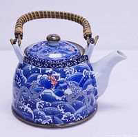 Front-side angle showing the blue and white porcelain with dragon and wave decoration and wicker handle on top.