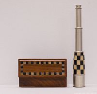 Photo showing the brass telescope extended next to the closed wooden case with checkerboard inlay on the lid.
