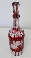 Front view of the cranberry glass decanter showing the etched floral and grapevine pattern with faceted stopper