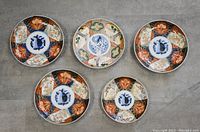 Top-down photo of 5 Chinese porcelain plates showing traditional hand-painted designs including alternating color panels with floral and geometric motifs.