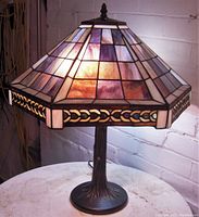 Front angled view of the lamp lit, showing the stained glass shade's color and design and the metal base.