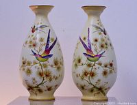 Pair of Crown Ducal English porcelain vases with colorful birds and pine branch motifs on creamy background. Both shown side by side.