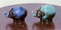 Side view of two elephant figurines, one blue and one greenish-blue, showing details and colors.