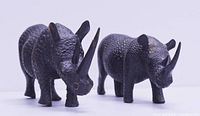 Front angled view of two dark stained carved wooden rhinoceros statues
