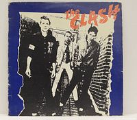 Front cover of The Clash vinyl LP showing band members in black and white with orange text and blue background, light edge wear visible.