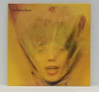 Front of album cover showing stylized blurry portrait of woman's face under translucent veil with yellow-orange background and title The Rolling Stones.